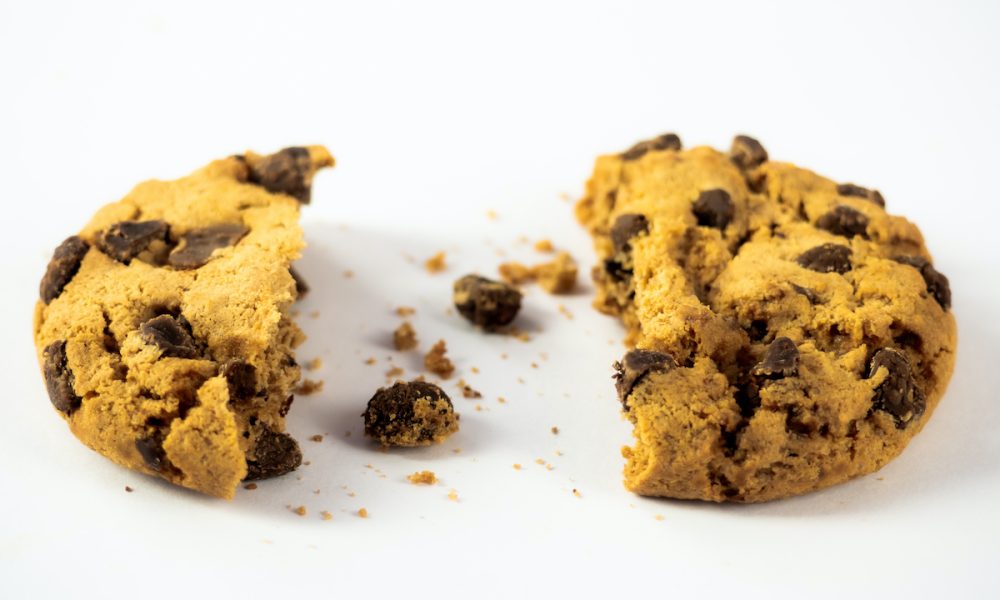 A homemade chocolate cookie with a bite and crumbs on a white background