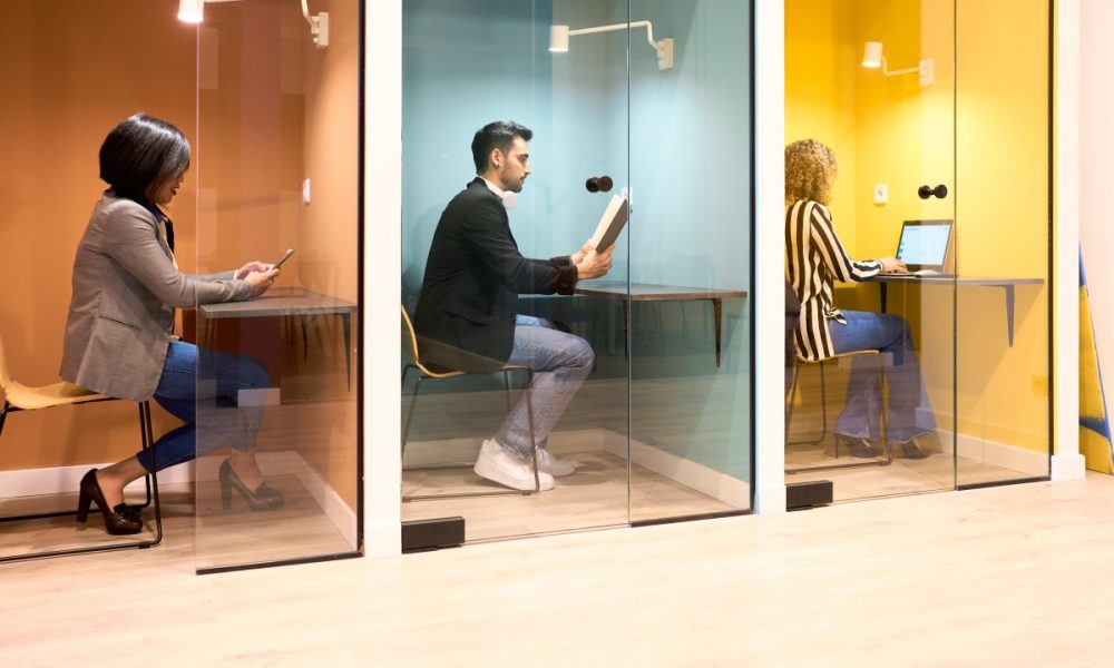 Train coworkers each sitting at the desk in their office cabin with a glass door, working