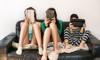 Three kids holding tablets sit on a couch