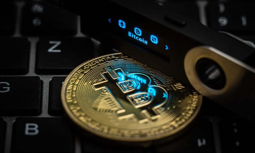 The word Bitcoin can be seen on the display of a Ledger Nano S hardware wallet next to a symbolic