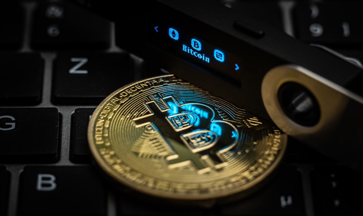 The word Bitcoin can be seen on the display of a Ledger Nano S hardware wallet next to a symbolic