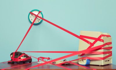 Image of a computer, phone and clock on a desk tied in red tape.